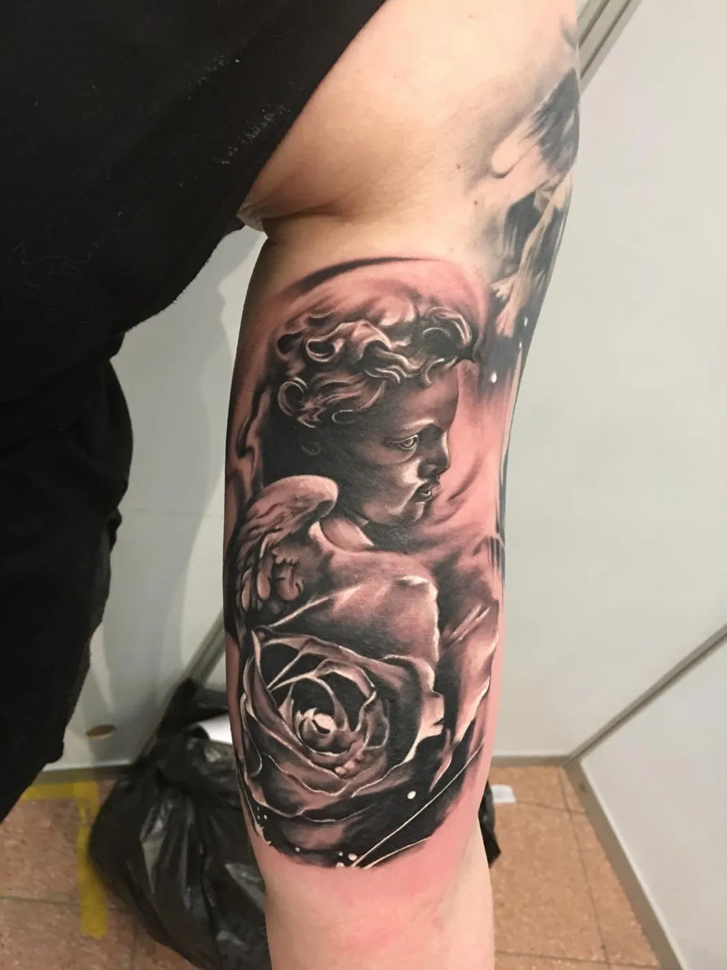 Putte mit Rose am Oberarm in weichem Black & Grey — Han, Alpenstich