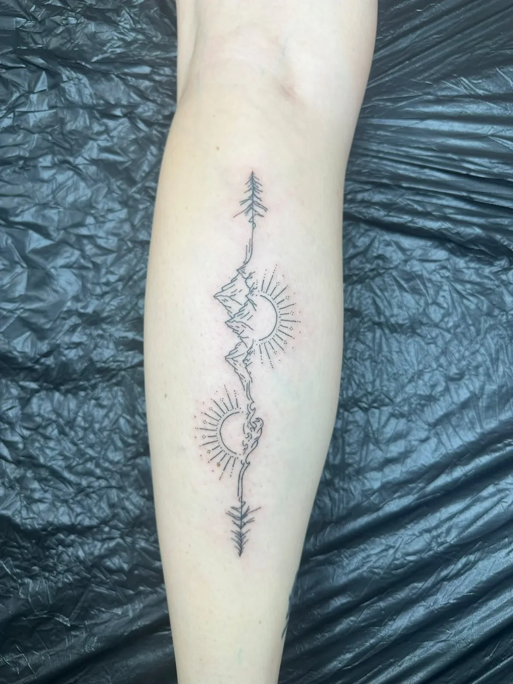 Feine Linienarbeit mit Bergen, Sonne, Mond und Tannen an der Wade — Tschenky, Alpenstich
