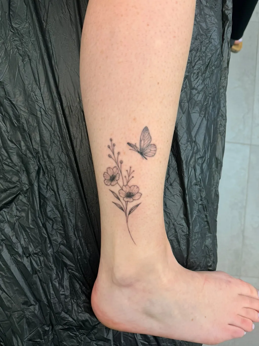 Feine Blumen mit Schmetterling am Knöchel im Fineline-Stil — Tschenky, Alpenstich